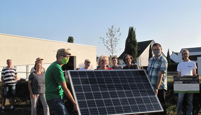 Zwei Männer halten ein Solarstrom-Modul, dahinter versammeln sich BUND-Mitglieder und Gäste.