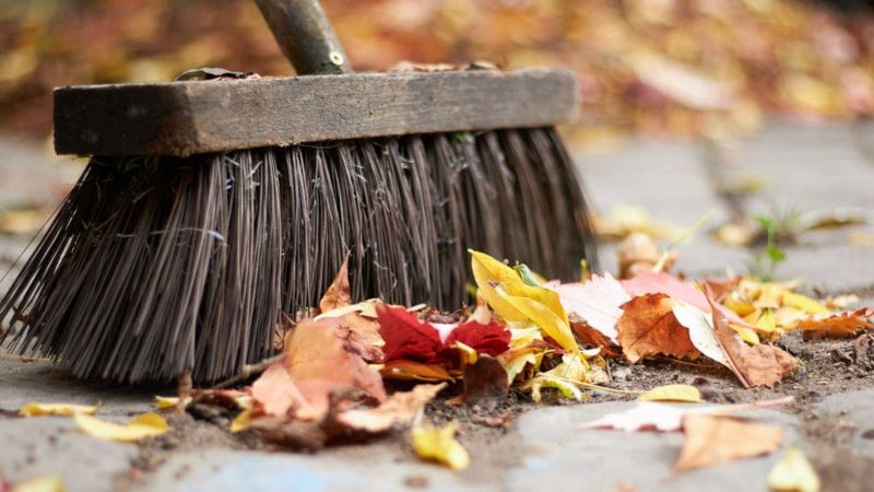 Herbstlaub mit Straßenbesen wegkehren