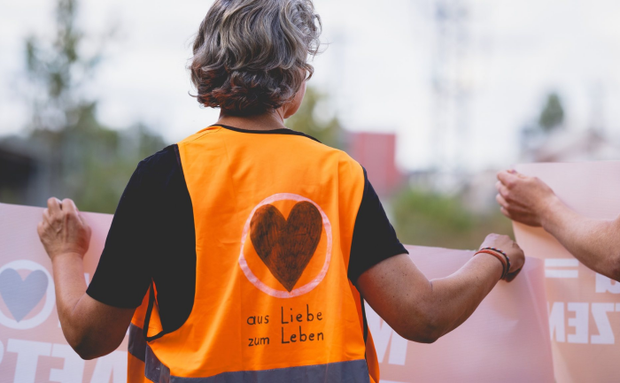 Mitglied der Letzten Generation beim Klimaprotest von hinten, die Warnweste träft die Aufschrift "Aus Liebe zum Leben".
